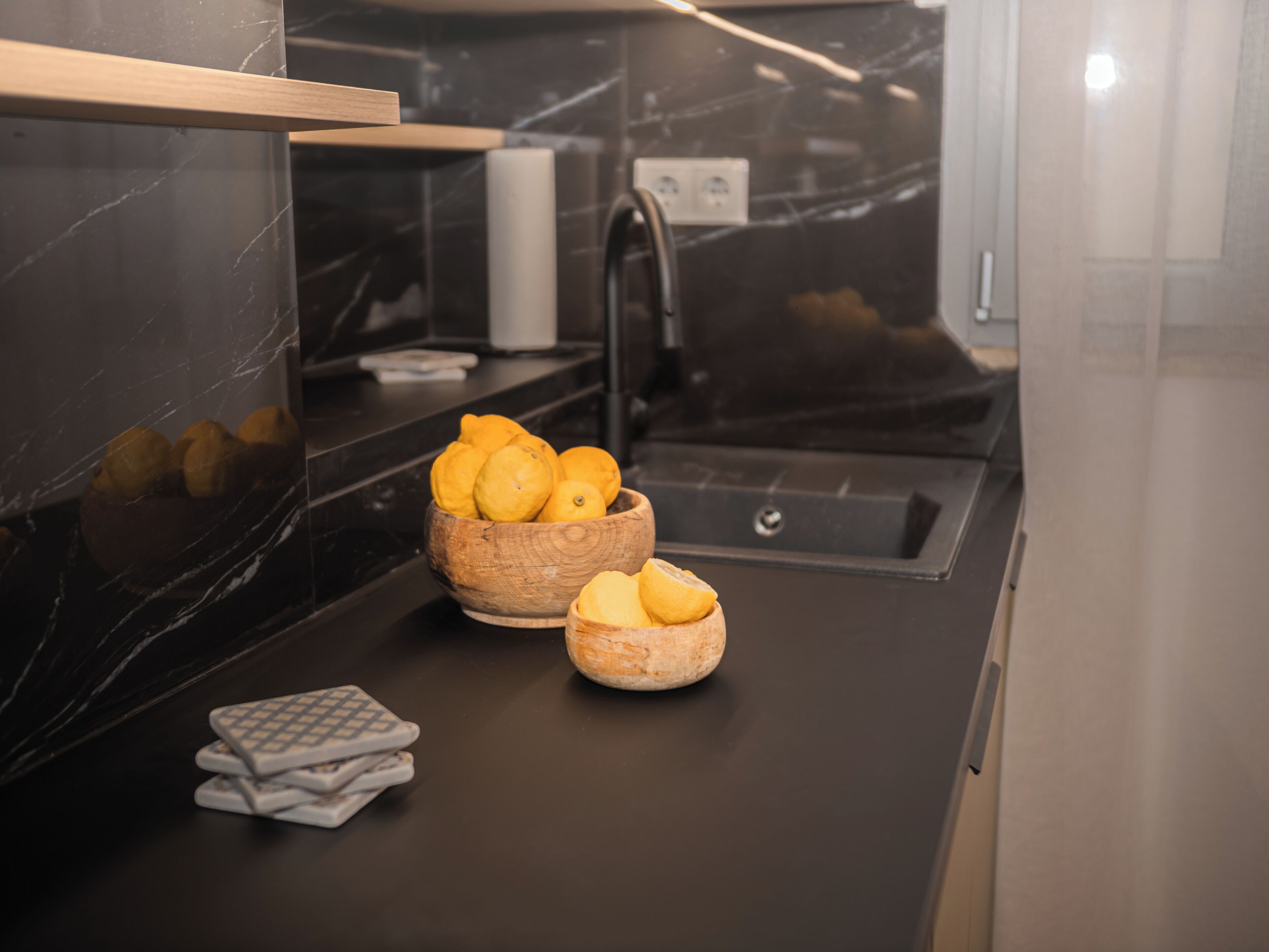 Una cocina con encimera de mármol, un cuenco de madera con limones y un lavamanos.