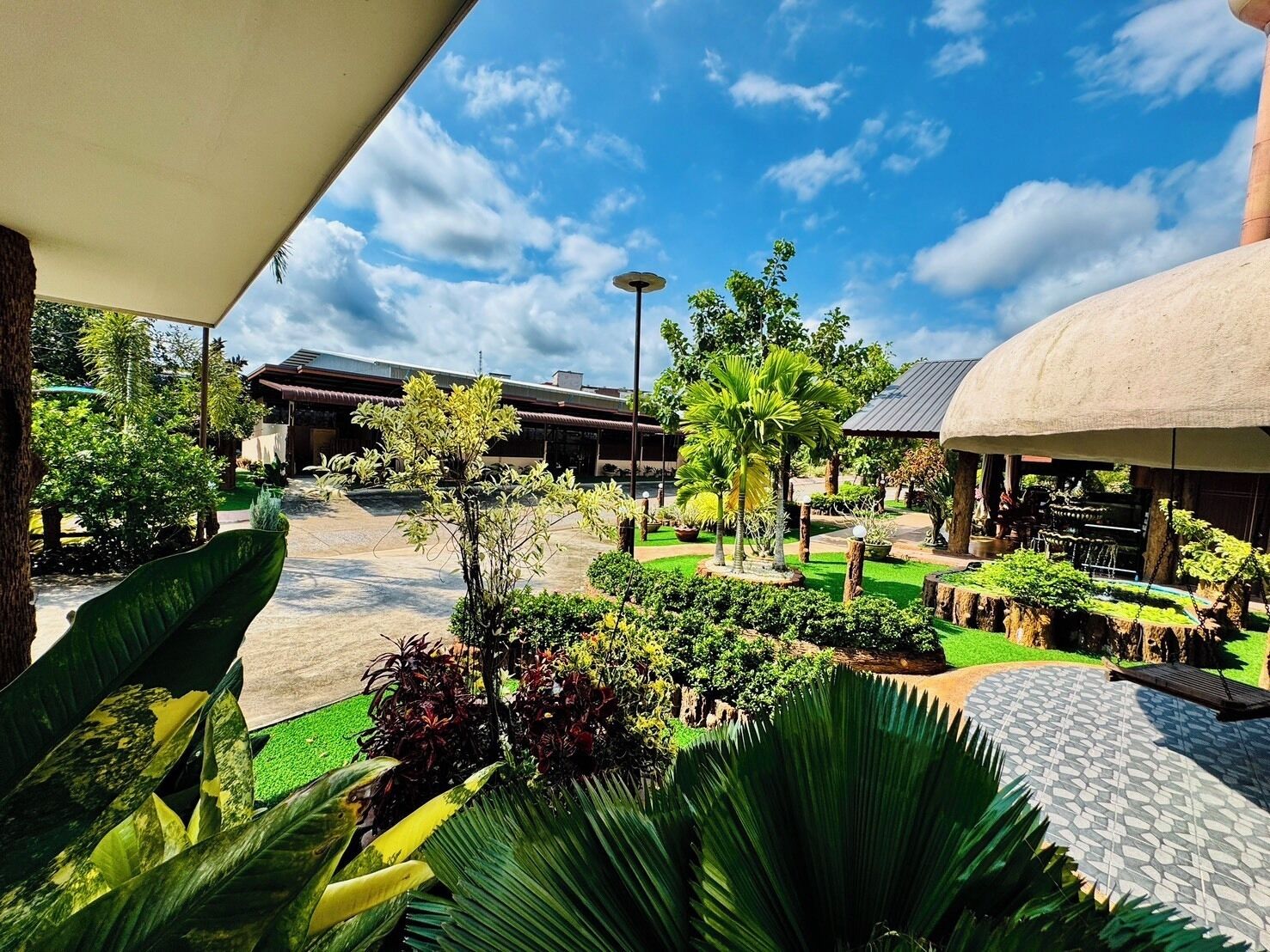 A courtyard with a building, palm trees, and a covered seating area.