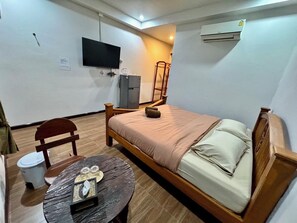 A compact room with a bed, a television, a small table with glasses, a chair, and a refrigerator.