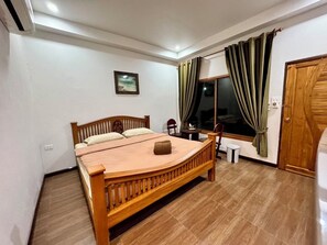 Un dormitorio con cama de madera, una mesita, una silla, una ventana con cortinas y una puerta.