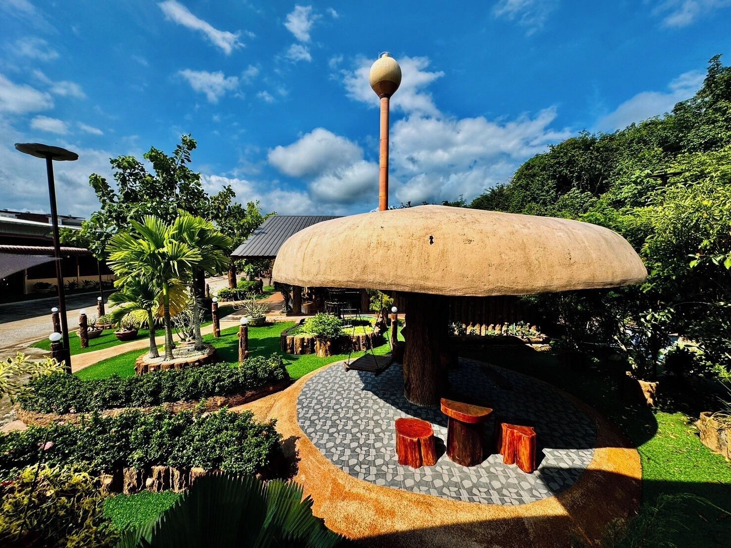 A large mushroom-shaped structure with a spherical top, surrounded by a landscaped garden with various plants and a paved walkway.