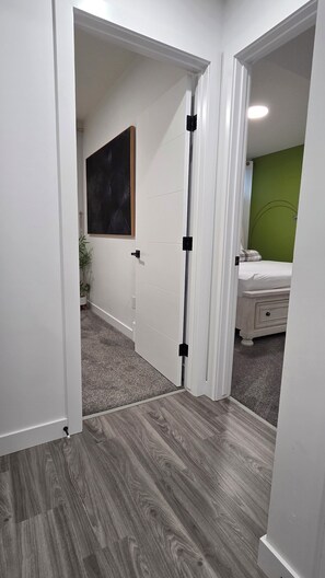 Ein Flur mit einer weißen Tür, einer grünen Wand und einem Bett, dessen Hintergrund ebenfalls eine grüne Wand zeigt.
