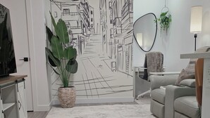 A living room with a large wall mural, a sofa, a coffee table, a TV, and a potted plant. - Cozy 2BR 14mins YYC Airport, University, Banff, Canmore & Entire Home Soft Water (Calgary)
