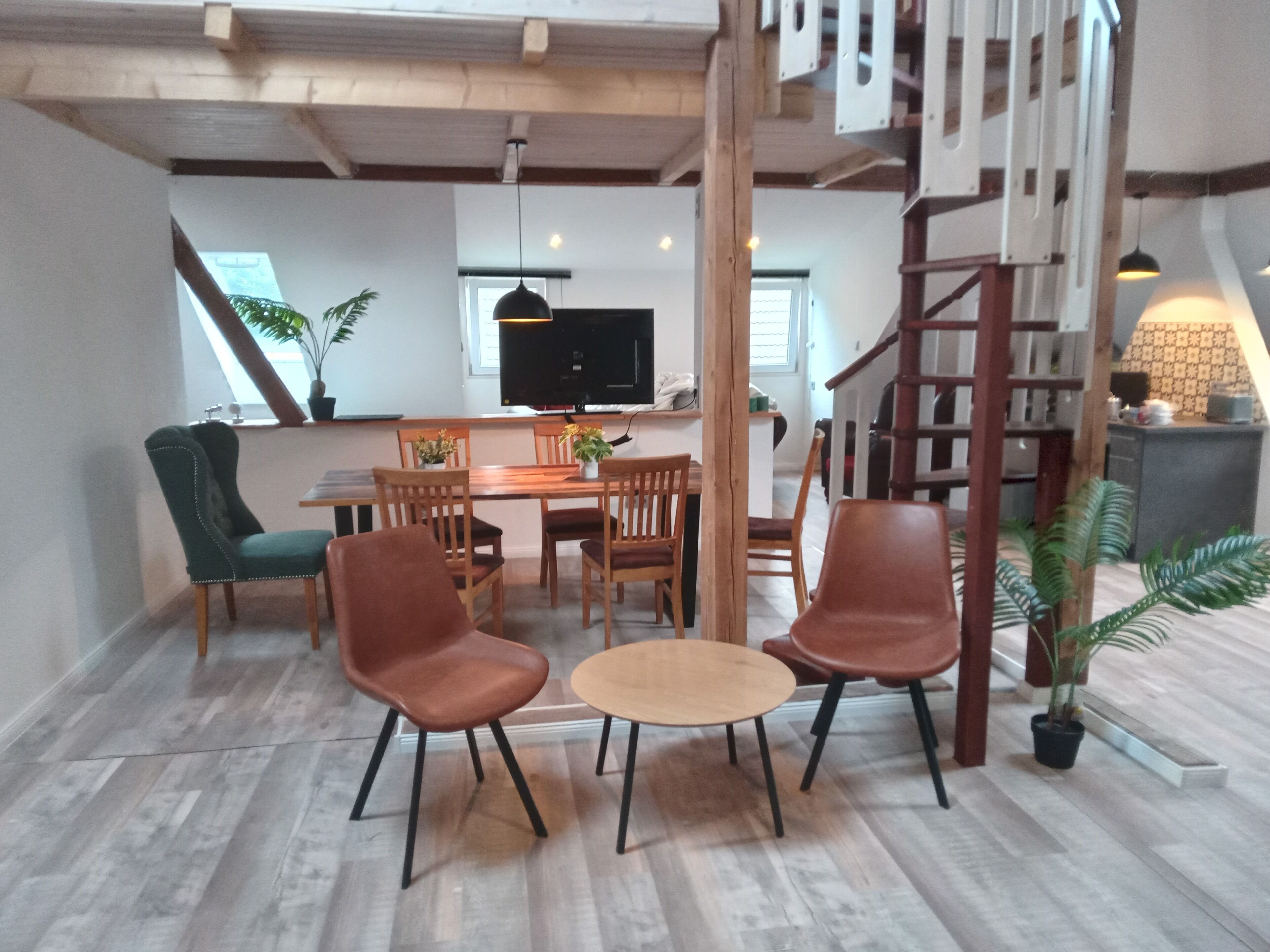Ruokailutila, jossa on puinen pöytä ja tuolit, televisio ja portaikko.