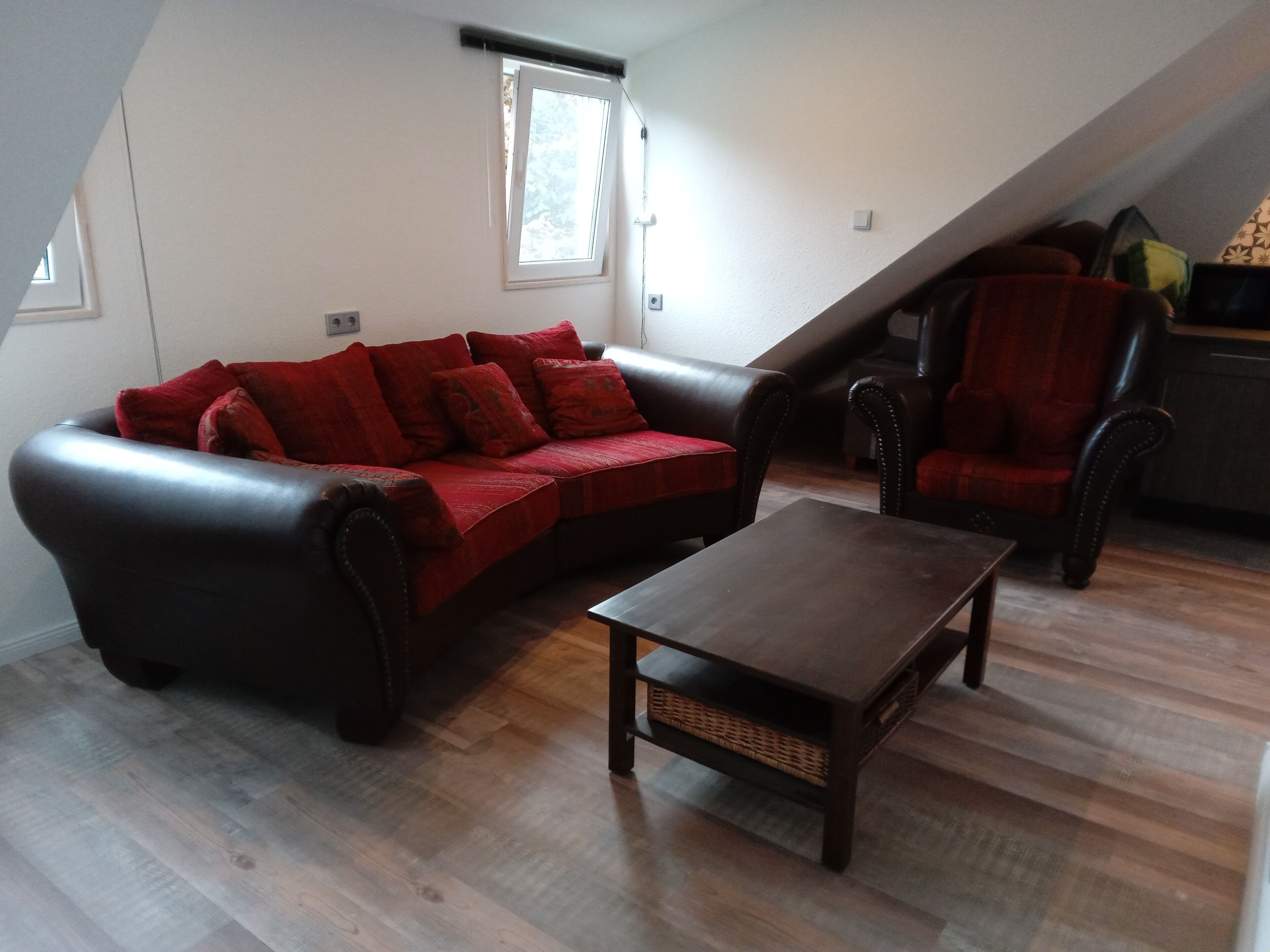 Ein Wohnzimmer mit einem dunkelbraunen Ledersofa, einem Holztisch und einer roten Decke.