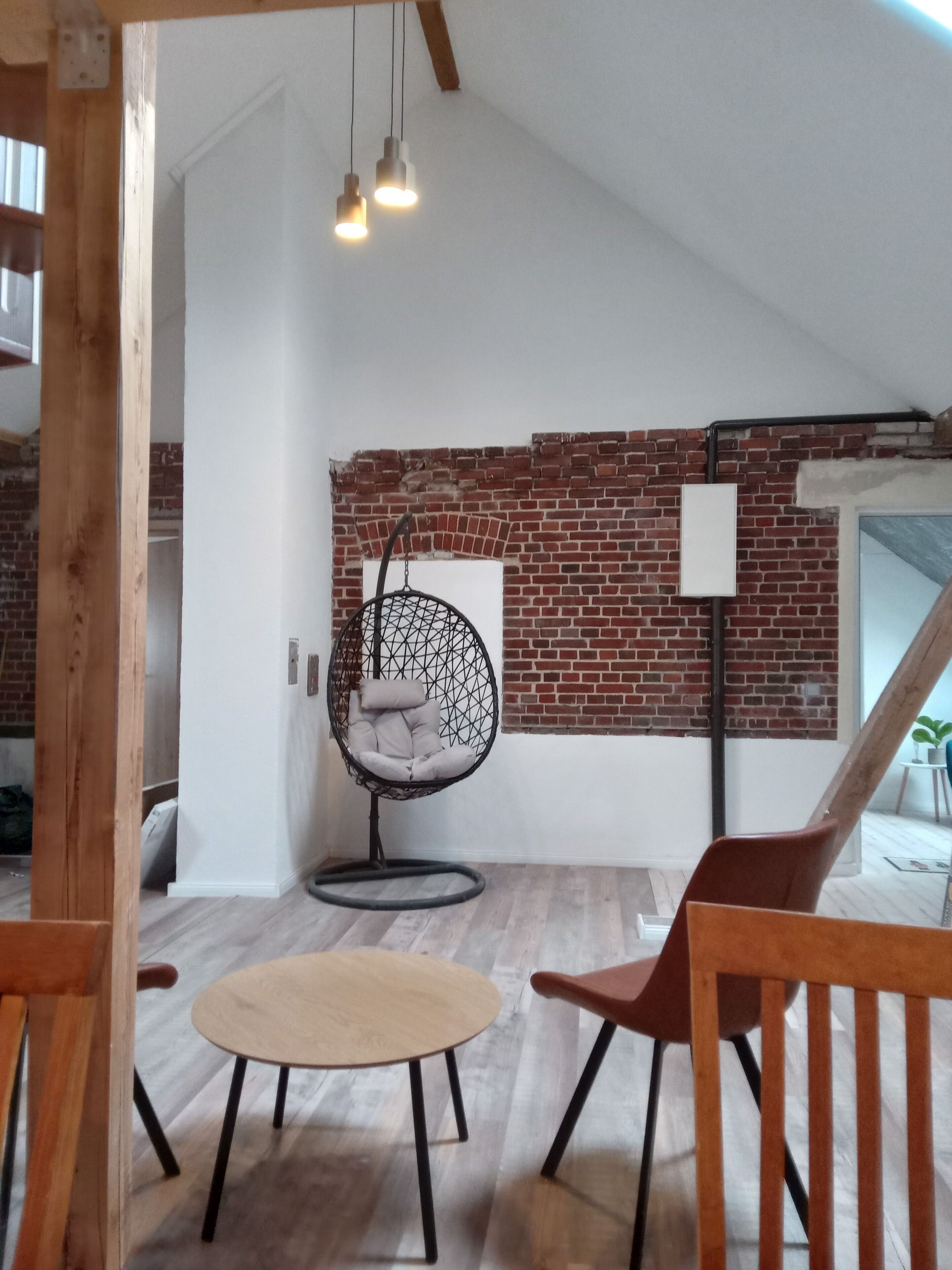 A room with a brick wall, a hanging chair, a wooden table, and a wooden chair.