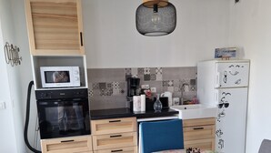 Una cucina compatta con forno a microonde, forno e macchina da caffè, un'area pranzo con tovaglia floreale e una sedia blu.