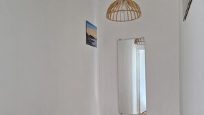 Un corridoio con pavimento in legno, un lampadario a sospensione, una parete bianca con un quadro incorniciato e un cestino bianco.