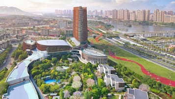 A modern urban area with a prominent tower, a curved building with a pool, and a well-maintained park with trees and a bridge.