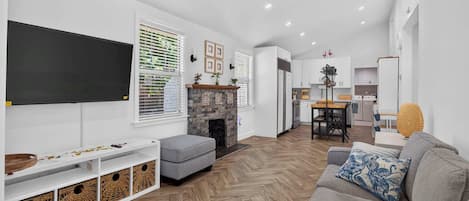 A modern living room with a fireplace, a flat-screen TV, and a herringbone-patterned floor.