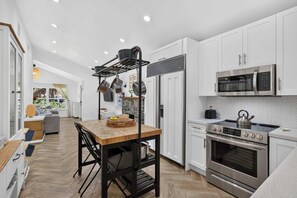 A modern kitchen with white cabinets, a wooden dining table, and stainless steel appliances.