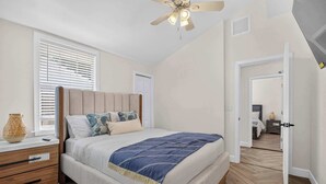 Een slaapkamer met een bed, nachtkastje en plafondventilator.