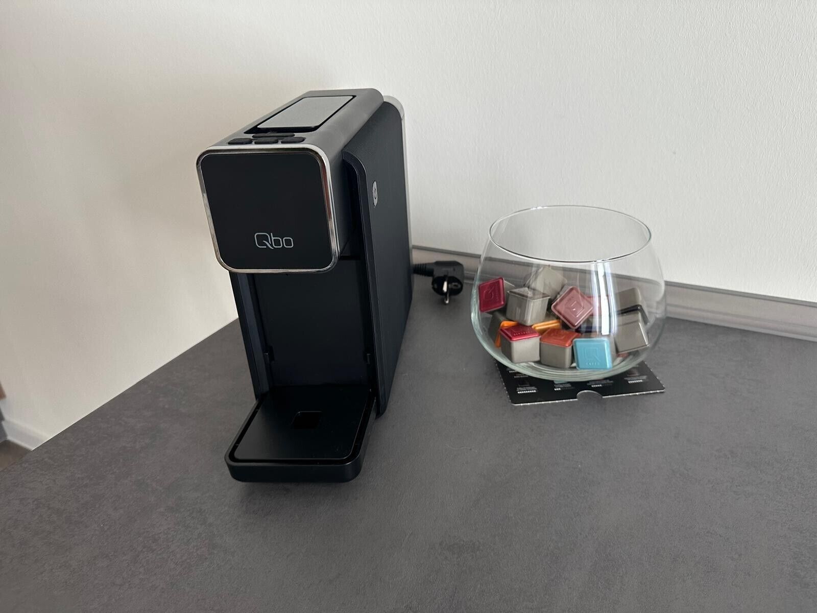 En kaffemaskine med et glas på disken, fyldt med kaffekapsler.