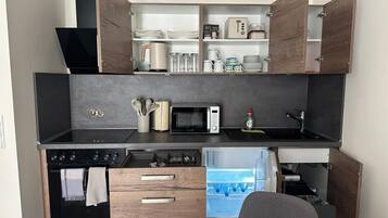 A compact kitchen with a built-in oven, microwave, and refrigerator, featuring wooden cabinetry and a black countertop.