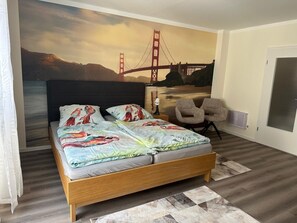 Un dormitori amb un llit, una cadira, un mural a la paret del Pont Golden Gate i una porta.
