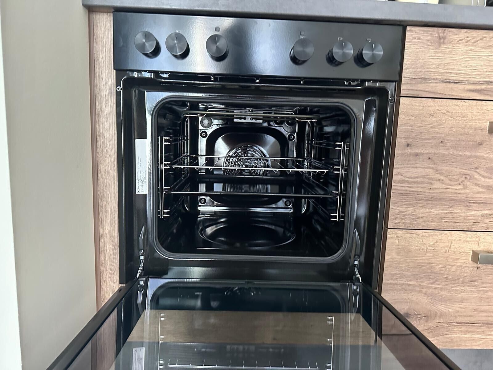 Ein offener Ofen mit Bedienfeld und einem Holzschrank im Hintergrund.
