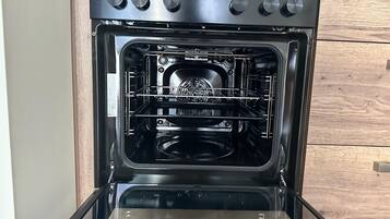 An open oven with a control panel and a wooden cabinet in the background.