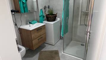 A modern bathroom with a glass shower enclosure, a white sink, a wooden vanity, and a small potted plant.