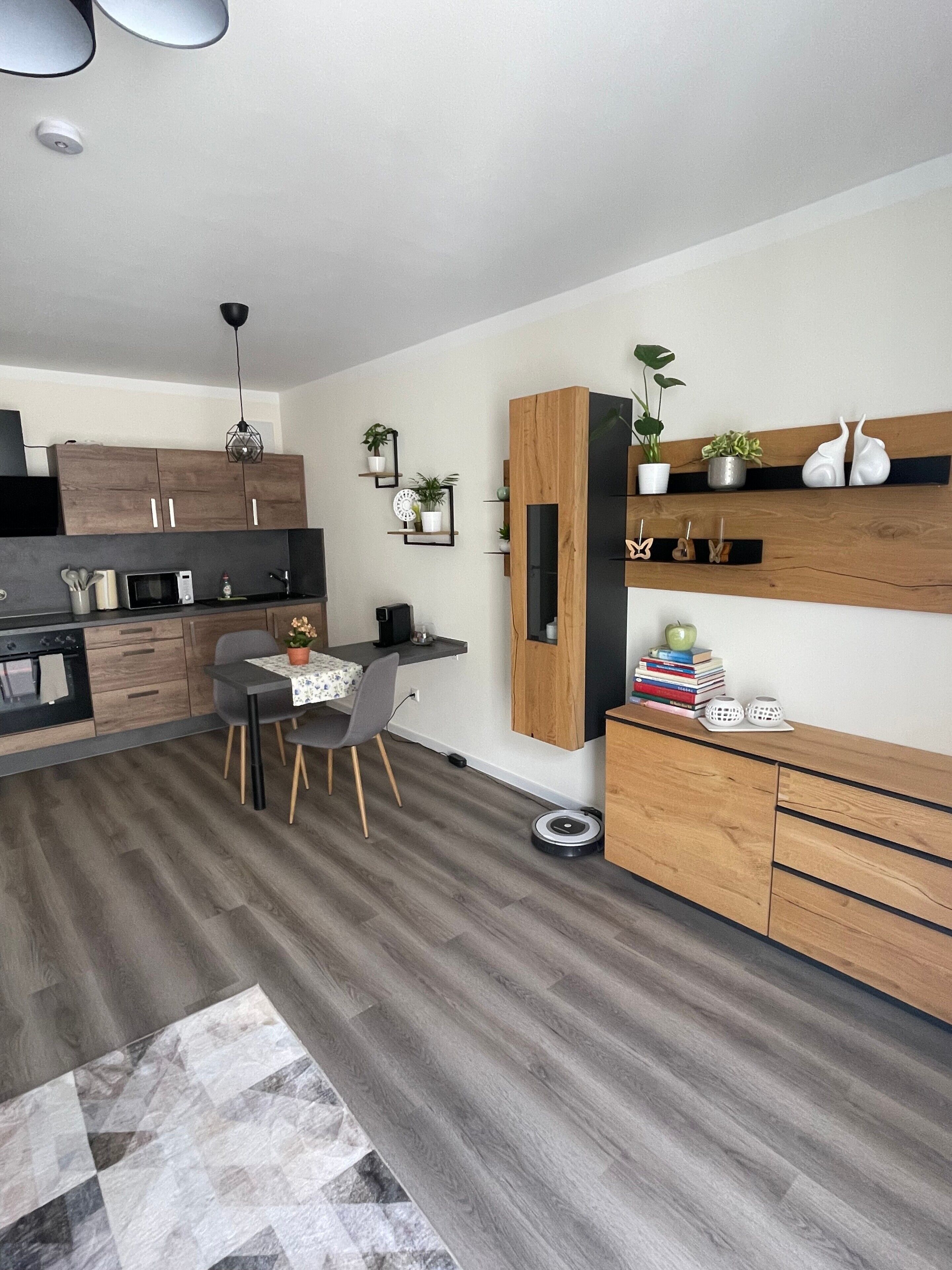 Eine moderne Küche mit Holzschränken, einem Essbereich mit Tisch und Stühlen sowie einem eingebauten Regal mit Pflanzen.