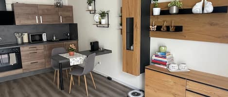 A modern kitchen with wooden cabinets, a dining area with a table and chairs, and a built-in shelf with plants.