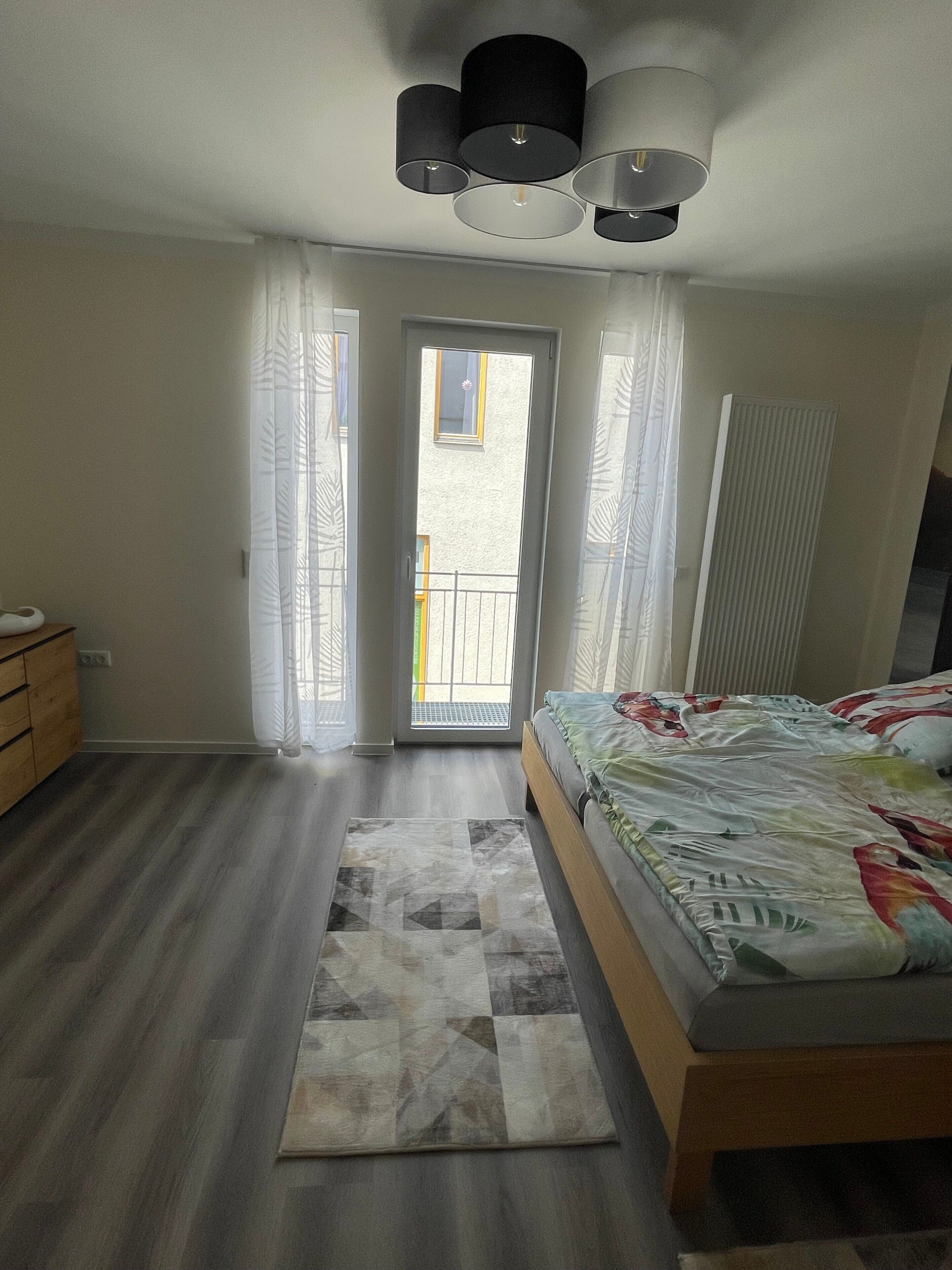 Een slaapkamer met een bed, een houten dressoir, een radiator en uitzicht op buiten door een deur.