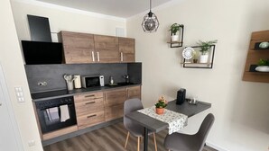 A modern kitchen with wooden cabinets, a microwave, and a dining area with a table and chairs. - Studio Apartment 'Lucas' Neudietendorf with Wi-Fi (Nesse-Apfelstädt)