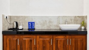 A bathroom with a black countertop, a white sink, wooden cabinets, a coffee maker, and a potted plant. - Hasthi Boutique Hotel (Kandy)