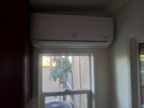 Ein Zimmer mit Fenster, einer darüber angebrachten Klimaanlage und einem Blick auf eine Pflanze vor dem Fenster.