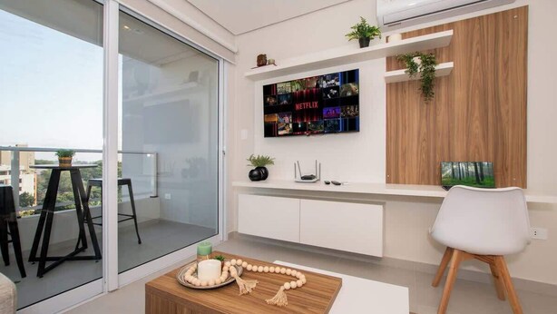 Ein modernes Wohnzimmer mit Glastür, einem Wand-Fernseher, einem Holztisch und einem weißen Sessel.
