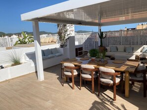 Eine Terrassenausstattung im Freien mit einem Holztisch und -stühlen, einem weißen Sofa und Topfpflanzen.