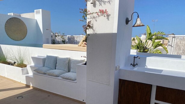 Eine Dachterrasse mit einer weißen Couch, einem fest montierten Waschbecken und einer Dekoglocke.