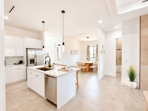 A modern kitchen with white cabinetry, a central island, and pendant lighting. - The Water Lily | Modern Waterfront Pool Home (Cape Coral)