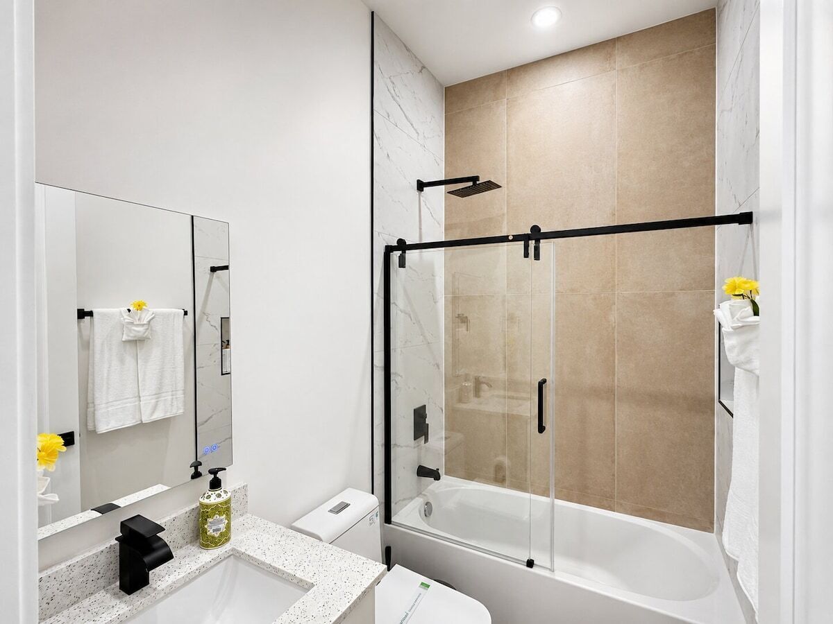 A modern bathroom with a glass-enclosed shower, a white sink with a marble countertop, and a large mirror.