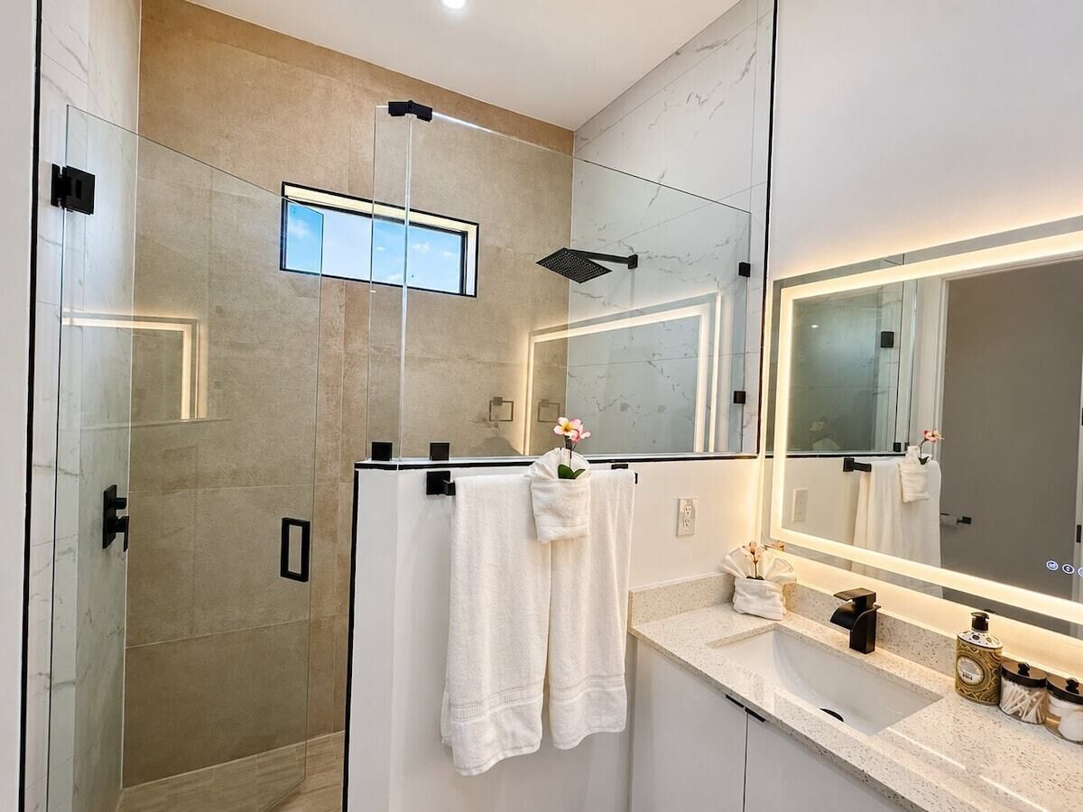 Een moderne badkamer met een douchecabine van glas, een grote spiegel en een wastafelmeubel met een aanrechtblad.