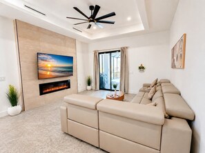 Ein modernes Wohnzimmer mit Sofa, Flachbildfernseher, Kamin und Deckenventilator.