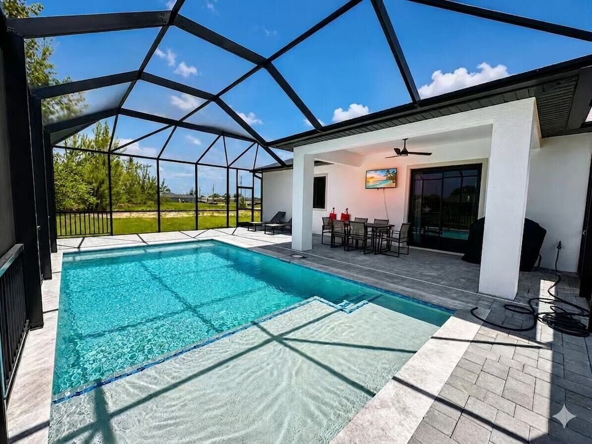Ein Schwimmbecken mit Glasdach, umgeben von einer Terrasse mit Gartenmöbeln.