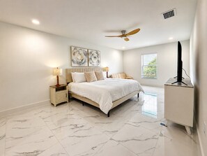 A bedroom with a bed, nightstands, a ceiling fan, a television, and artwork on the wall. - Palm Paradise on the Canal (Cape Coral)