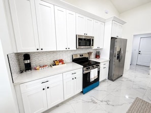 A modern kitchen with white cabinets, a black stove, a stainless steel refrigerator, and a microwave. - Palm Paradise on the Canal (Cape Coral)