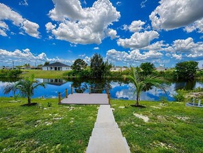 A pathway leading to a dock over a calm body of water, surrounded by greenery and a clear sky. - Palm Paradise on the Canal (Cape Coral)