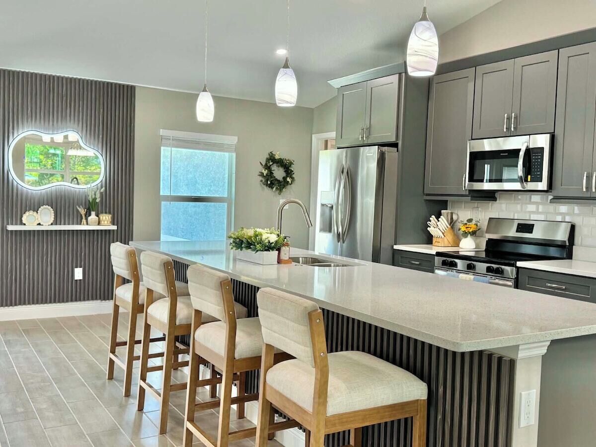 A modern kitchen with a central island, bar stools, stainless steel appliances, and pendant lighting.