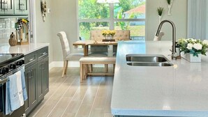A modern kitchen with a central island, a dining area with a bench, and a view of the outdoors. - Cape Coral Waterfront Oasis (Cape Coral)