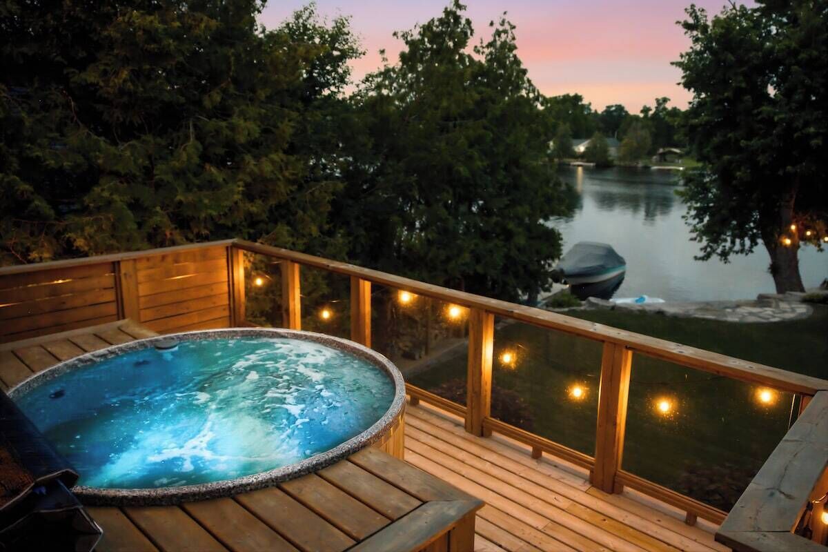 Une terrasse en bois avec un jacuzzi, donnant sur un lac bordé d’arbres et doté d’un quai.