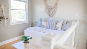 Un dormitorio con una cama, un tapiz de macramé, una ventana y una planta sobre una mesa.