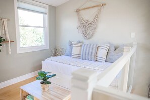 A bedroom with a bed, a macrame wall hanging, a window, and a plant on a table. - Cedar Barrel Lakehouse - Hot Tub|Water Toys|Views (Kawartha Lakes)
