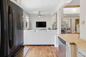 A modern kitchen with a built-in oven, a dining area with a stone accent wall, and a flat-screen TV mounted above the sofa. - Cedar Barrel Lakehouse - Hot Tub|Water Toys|Views (Kawartha Lakes)