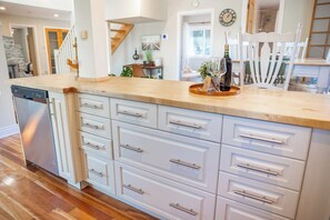 A kitchen with a dishwasher, white cabinetry, and a wooden countertop. - Cedar Barrel Lakehouse - Hot Tub|Water Toys|Views (Kawartha Lakes)