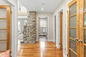 A hallway with wooden flooring, stone pillar, and wooden doors with glass panels. - Cedar Barrel Lakehouse - Hot Tub|Water Toys|Views (Kawartha Lakes)