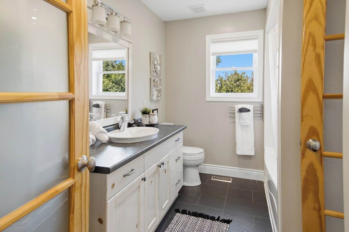 A bathroom with a white sink, a toilet, a shower, and a window with a view.