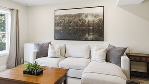 Una sala de estar moderna con un sofá grande, una mesa de centro con una planta y un cuadro en la pared.