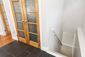A hallway with a wooden door with glass panels, a white wall, and a white staircase. - Cedar Barrel Lakehouse - Hot Tub|Water Toys|Views (Kawartha Lakes)